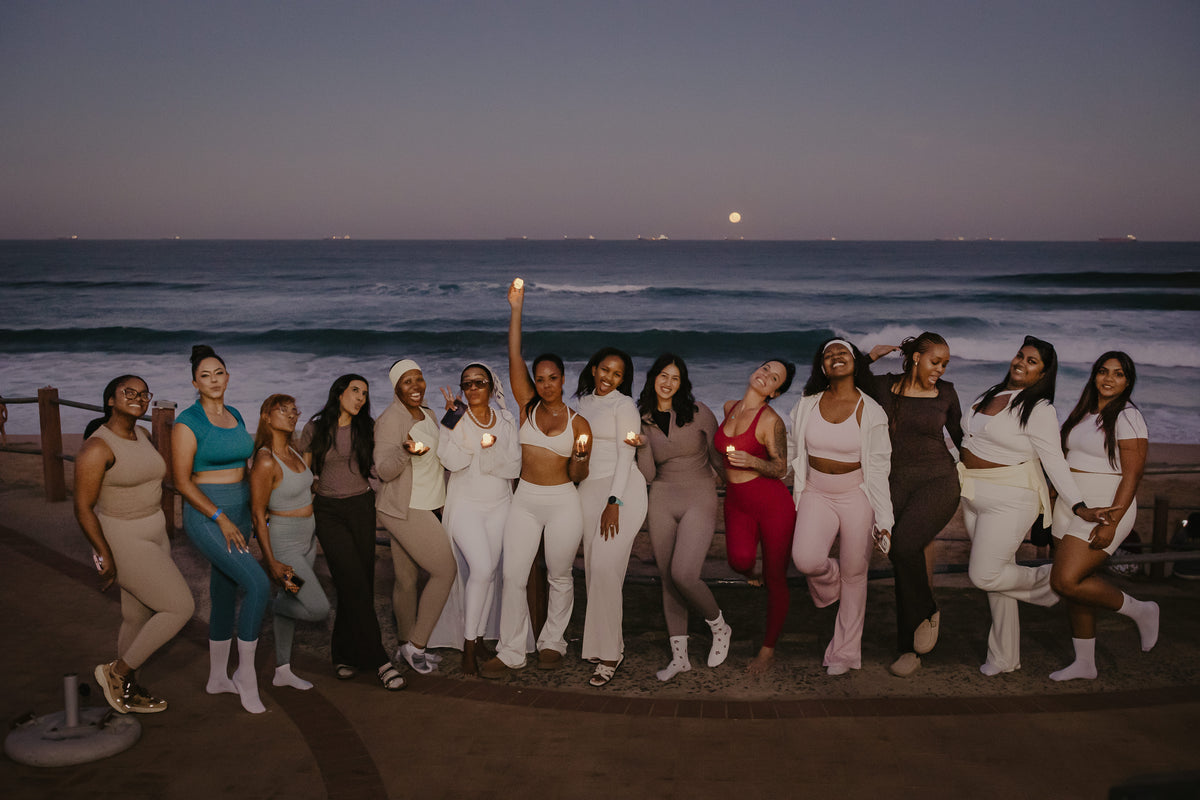 Women from the Reset With Abi community holding candles on the Durban beachfront at dusk